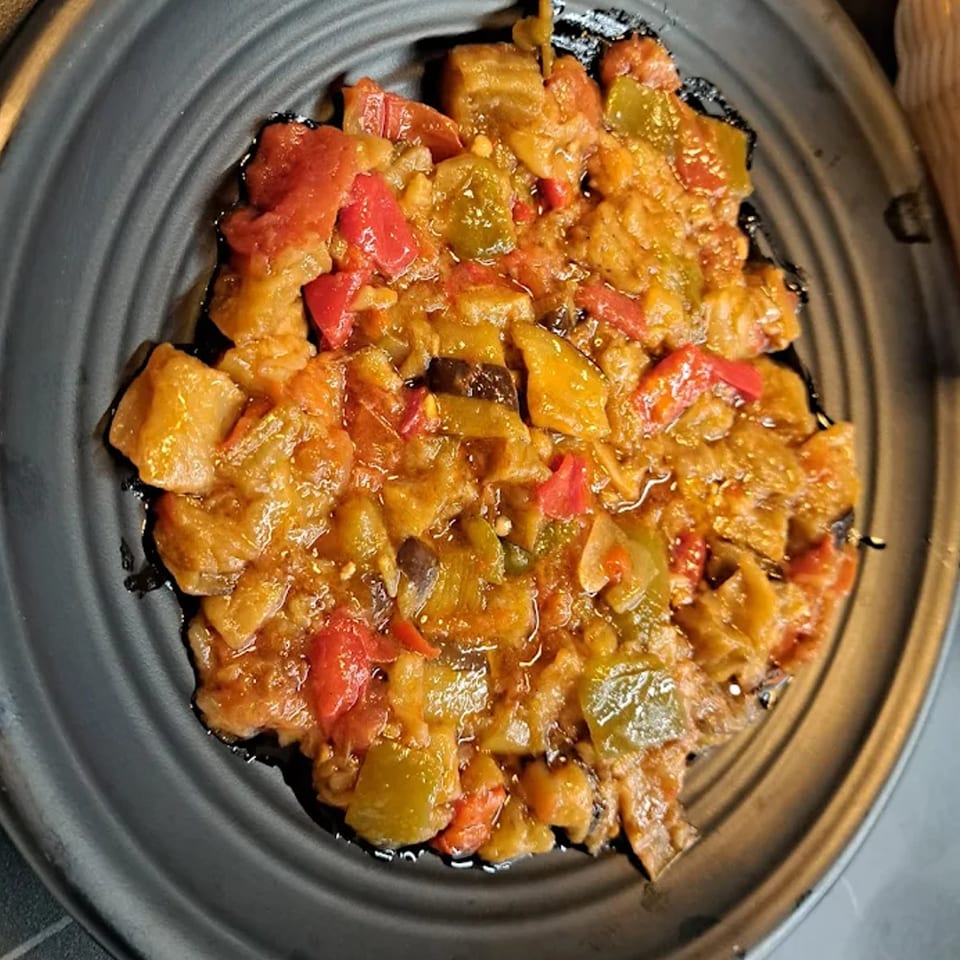 A close-up of a Turkish eggplant dish with red and green peppers on a dark plate.