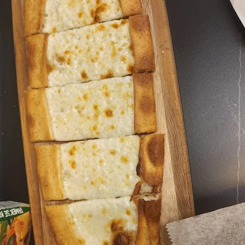 Turkish cheese pide, a flatbread topped with melted white cheese, sliced and served on a wooden board.
