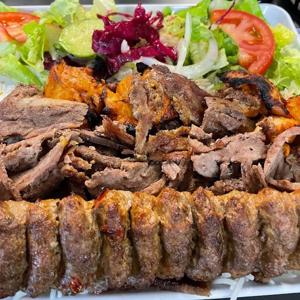 A Turkish mixed grill platter with sliced doner, chicken shish, adana kebab, rice, and fresh salad.