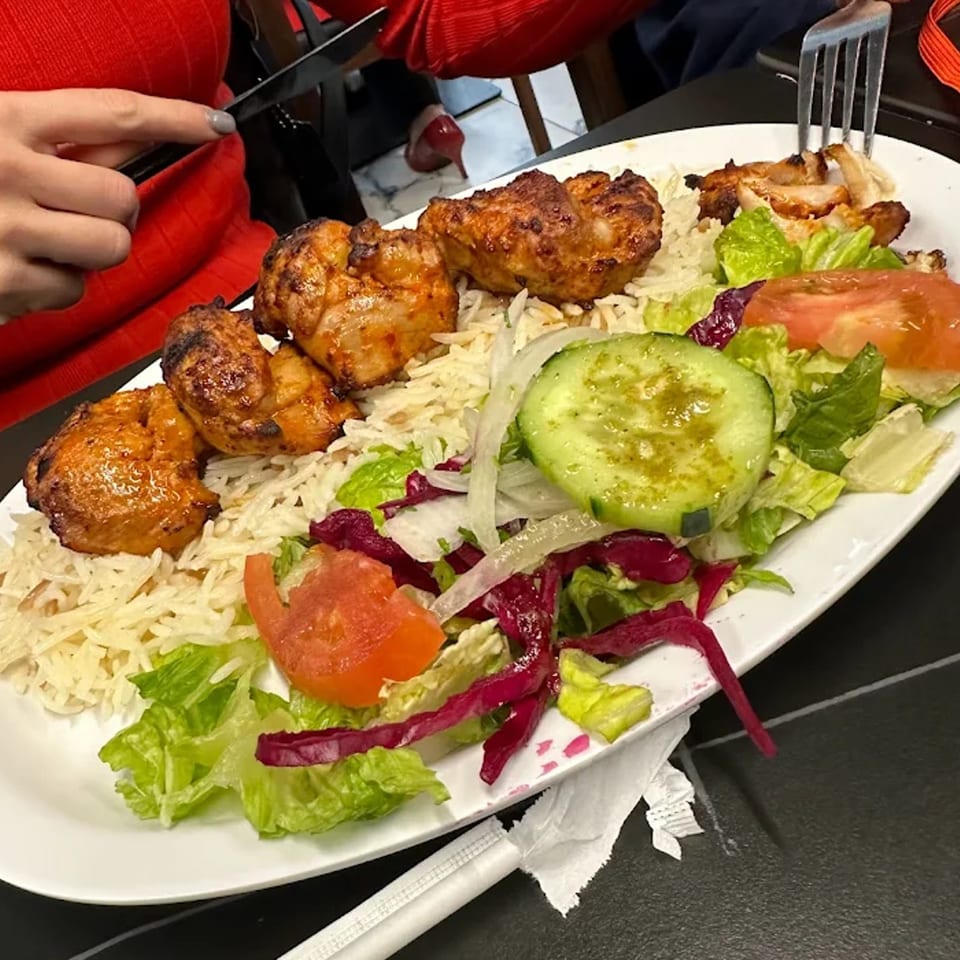 A Turkish chicken shish kebab plate with rice, salad, and a person cutting chicken.