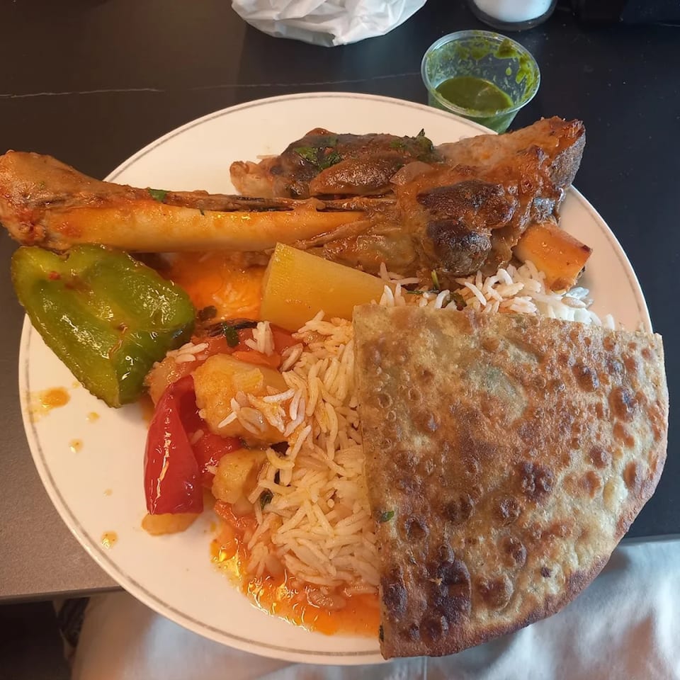 Turkish lamb shank with rice, vegetables, and flatbread on a white plate.